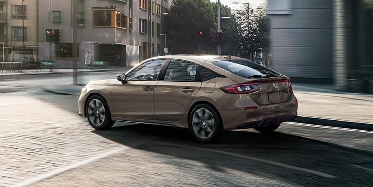 2027 Honda Civic Hatchback Sport Hybrid in Urban Gray Pearl back driving through a busy city street (Compact Hatchback).