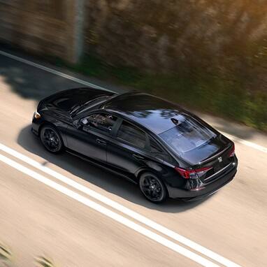 2027 Honda Civic Sedan Sport in Crystal Black Pearl high-angle rear three-quarter view driving on a road (Compact Sedan)